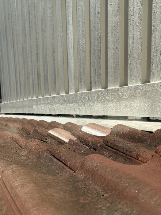 Tegelpannor av olika storlek på tak nära en vit vägg, där vissa nya pannor lyfter.