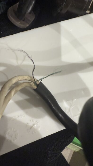 Tre vita elsladdar med avklippta ändar, synliga vita, gröna och blå koppartrådar, nära en svart kabel.