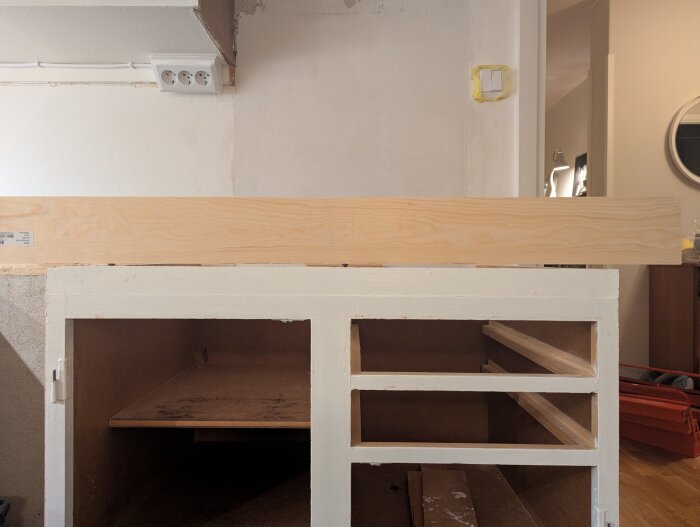 Köksmodul där diskmaskin ska stå, träsockel ovanpå och saknade lådor, väggkontakt till vänster, ljus vägg i bakgrunden.