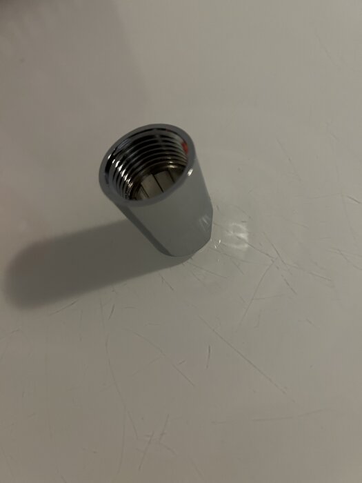 Metallhylsa för duschslang placerad på ljus yta, med invändig gänga synlig.