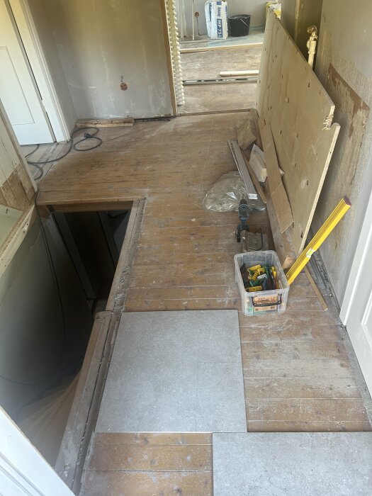 Hall med trägolv, några klinkerplattor på golvet, verktygslåda till höger, öppning mot vardagsrum i bakgrunden, trappöppning till vänster.