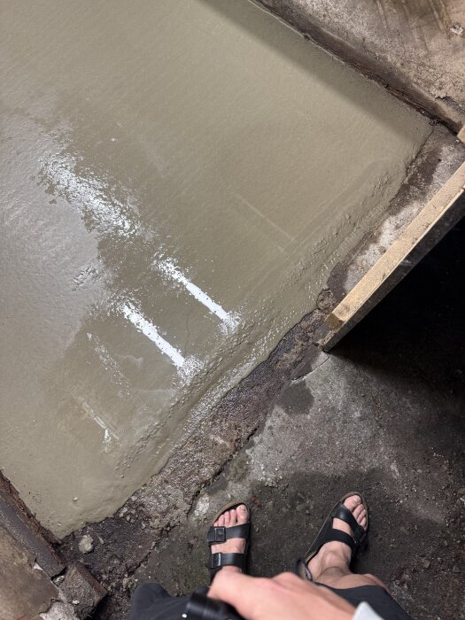 Gammal betongsula framför dörr, nyligen bearbetad. Synlig makadamkant bredvid. Person med sandaler syns delvis i bildens nederkant.