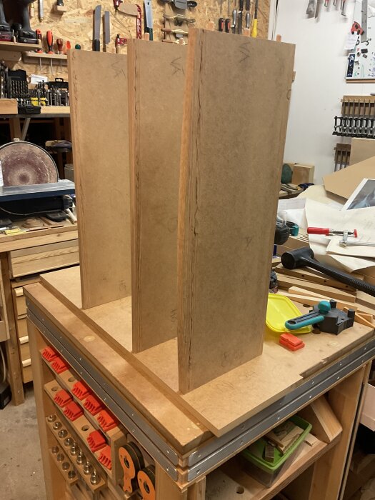 Träram av MDF-plattor uppställda på arbetsbänk i verkstad med diverse verktyg och tillbehör.