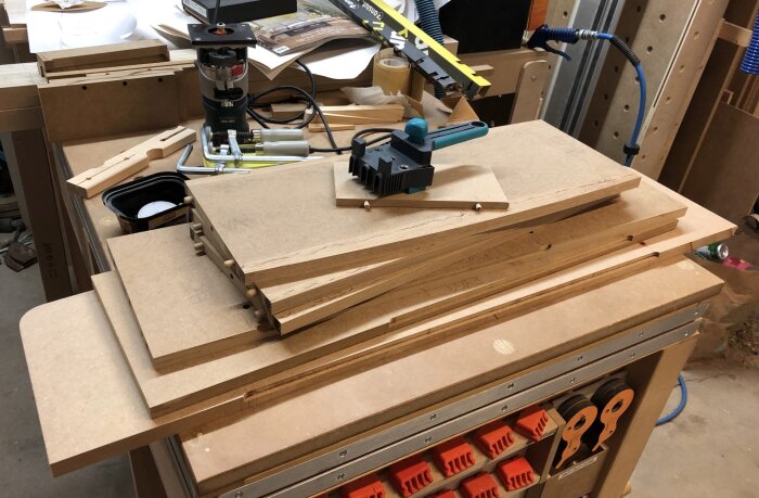 Arbetsyta med MDF-skivor och verktyg för bygge av sideboard, inklusive en Wolfcraft pluggjigg och borrmaskin på en verkstadsbänk.