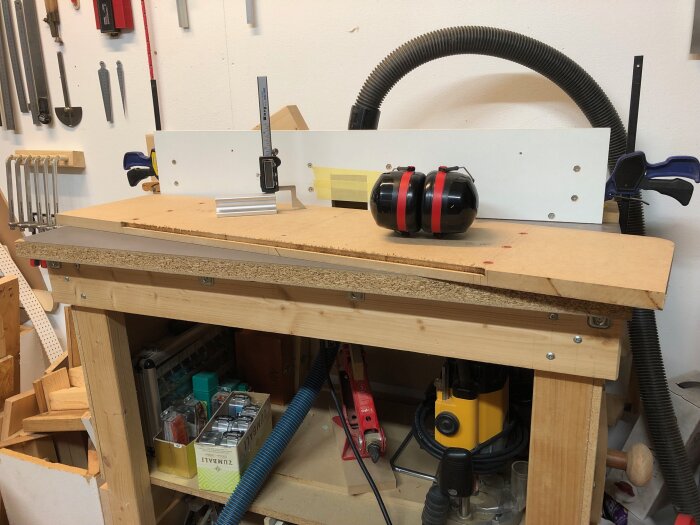 Arbetsbänk med fräsutrustning och skyddshörselkåpor i träverkstad.