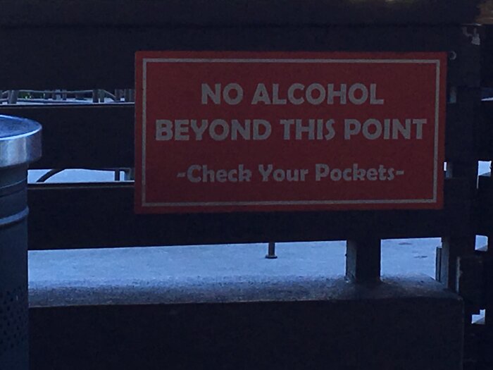 Skylt med texten "No alcohol beyond this point – Check your pockets" vid utomhusplats.