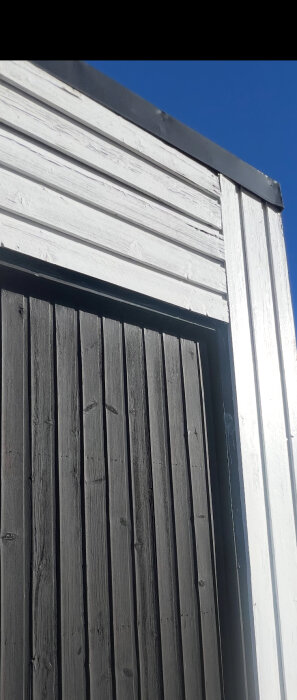 Bild av garagevägg med både liggande och stående panel, där den övre panelen är vit och den nedre är mörkare.