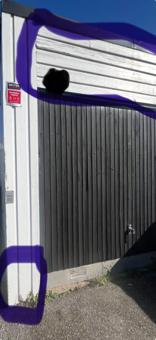 Garage med vit liggande och svart stående träpanel samt märkbar röta på vissa delar.