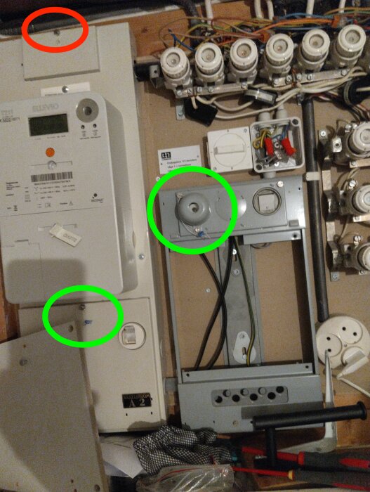 Elcentral med två plomberingar markerade i grönt och en saknad plombering högst upp markerad i rött, kablar och proppar synliga.