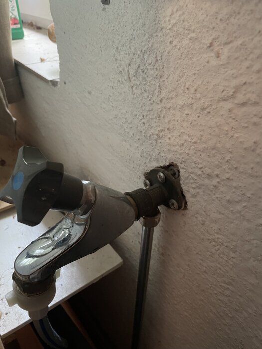 Gammal vattenkran med läckage synligt vid den sexkantiga delen och slitet väggfäste på grov vägg.