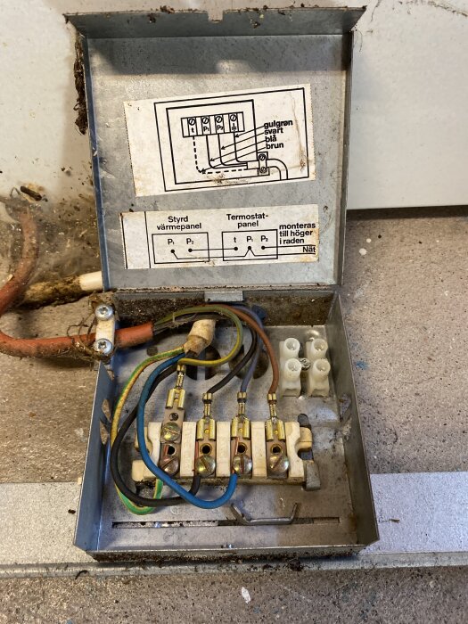 Elektrisk kopplingsdosa med fyra kablar: gul/grön, blå, svart och brun. Diagram på insidan visar kabelanslutningar. Brun kabel är bortklippt.