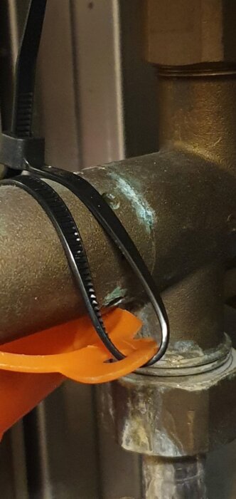 Läckande rör i fjärrvärmecentral med tratt och slang för vattenavledning, ombunden med buntband, antyder reparation.