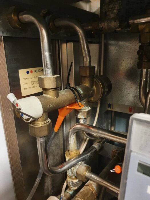 Rör i fjärrvärmecentral med tratt och slang monterad för att hantera vattenläckage. Silverrör och ventiler syns i en gammal central.