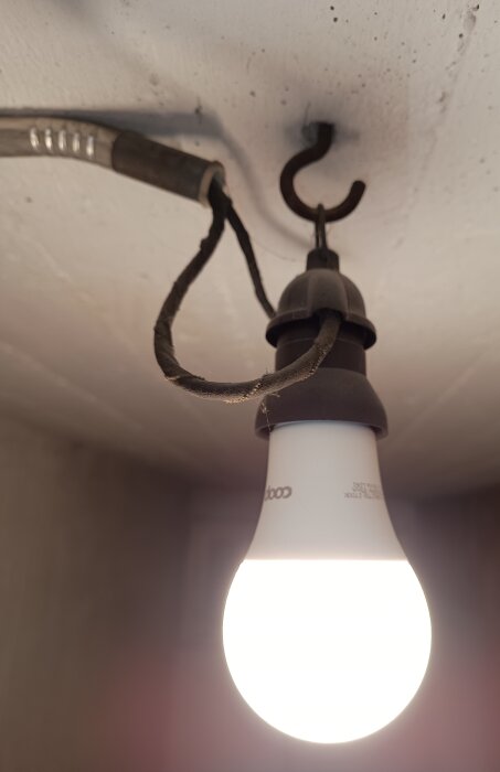 Äldre taklampa från 1946 med synlig glödlampa och sladd inspunnen i kroken i taket.