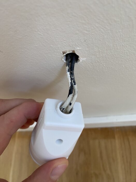 Elkablar och uttag monterade på vägg, med vit och svart kabel dragna ur ett hål, hållna av en hand.