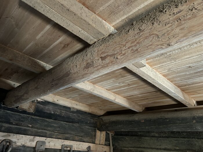 Ett tak med träplankor och en stödbjälke synlig i en gammal ria, med en bjälke som ser ut att ha blivit bytt.