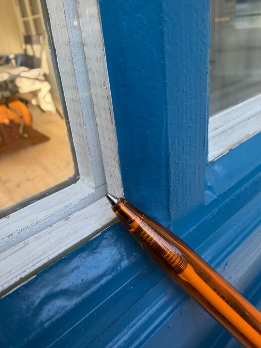 Penna pekar på fönsterkarmens skarv vid en blåmålad träbåge, diskuterar luftningshål mellan fönsterbågar.