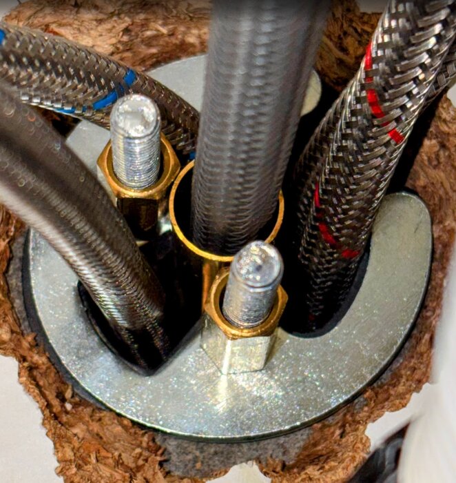 Två metallstänger med muttrar monterade på diskbänksplatta, omgivna av flexibla flätade vattenrör, installation av köksblandare.