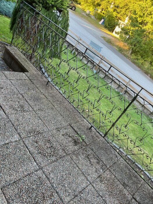 Smidesräcke fastskruvat och gjutet i plattor, med natur och väg i bakgrunden. 895 cm långsida, 151,5 cm kortsida, 100 cm högt.