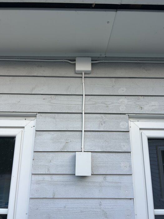 Fasad med vitmålad vägg och elkablar, nära ett fönster.
