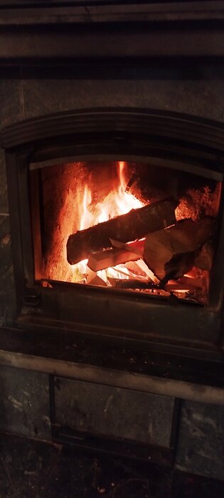 Vedeldad brasa i en öppen spis, med synliga lågor och vedträn.