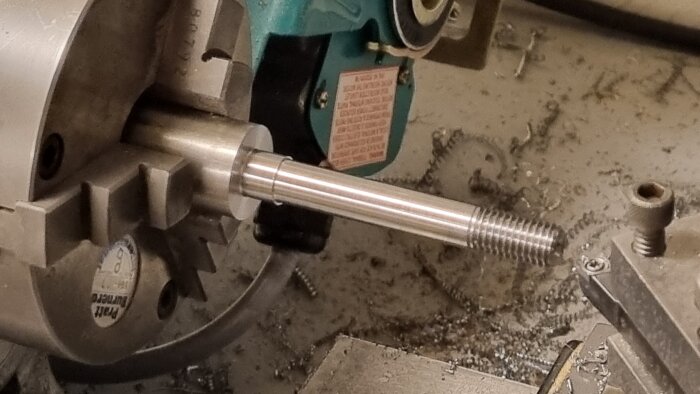 Svarvad metallstång i svarv med gängad ände, omgiven av metallspån och verktygsdelar.