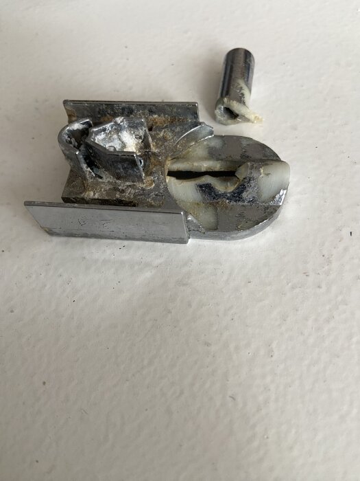 Trasigt lyftgångjärn för duschdörrar från cirka 2016, med en avbruten del, placerat på en ljus yta.