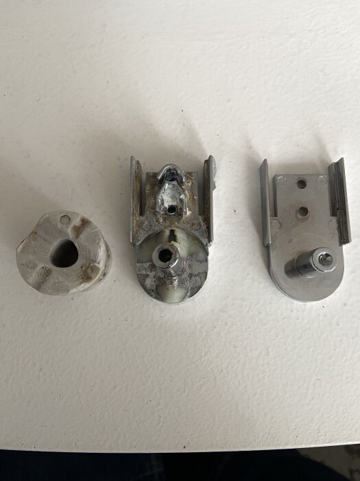 Tre delar av ett trasigt lyftgångjärn för duschdörrar från cirka 2016, placerade på en vit yta.