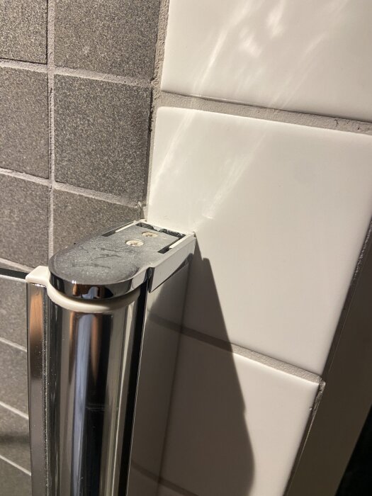 Lyftgångjärn på duschdörr mot kakelvägg, sönder del synlig.