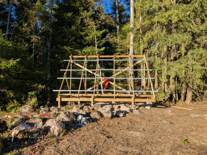 Markställning för solceller i skogsmiljö med person i orange kläder, omgiven av stenar och träd.