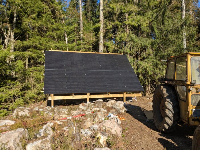 Solpaneler på markställning i skogsmiljö med en traktor bredvid, en del av hemmaprojekt för solenergiinstallation.