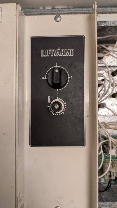 Termostat för luftvärmesystem med varvtalskontroll och temperaturratt, omgiven av synliga elektriska komponenter och kablar.