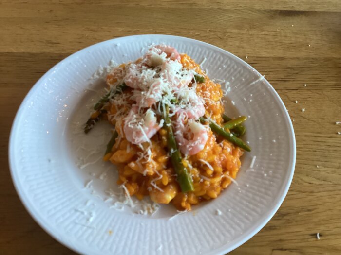 Saffransrisotto med sparris, räkor och riven ost på en vit tallrik.