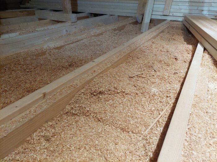 Träbjälklag täckt med kutterspånsisolering som har sjunkit ihop något, synligt i ett pågående renoveringsprojekt för vinden.