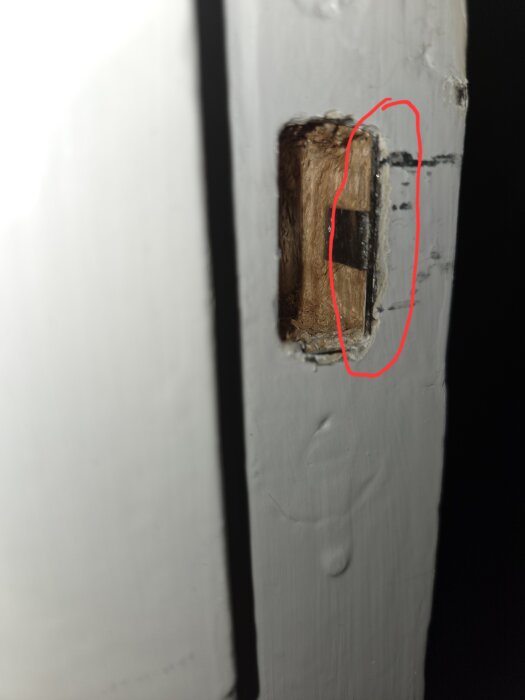 Närbild av dörrkarm med urgröpt hål och markerad metalldel för låsjustering.