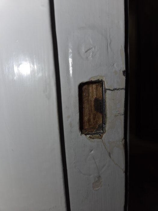 Närbild av en dörrkarm med ett ovalt hål, tecken på tidigare reparationer, behöver målas om.