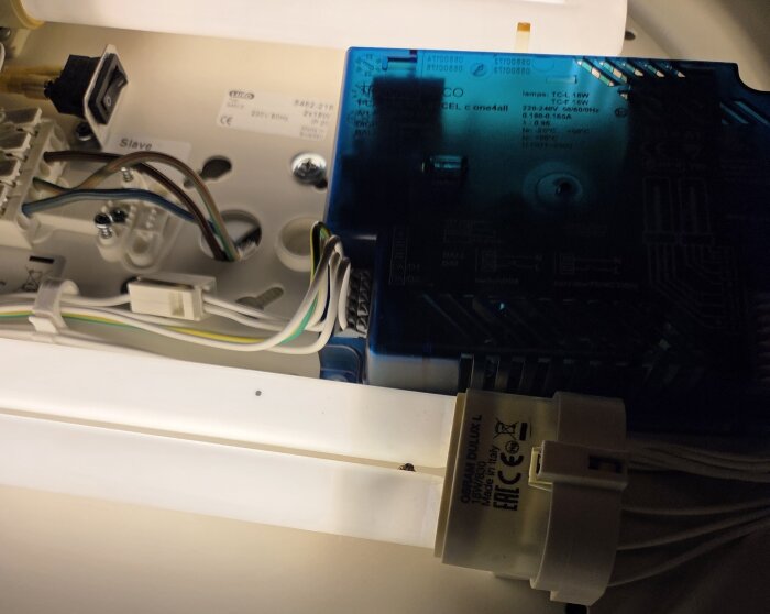 Närbild av en Osram Dulux L 18W 830 lysrörslampa installerad i en armatur med omgivande elektriska komponenter och kablar.