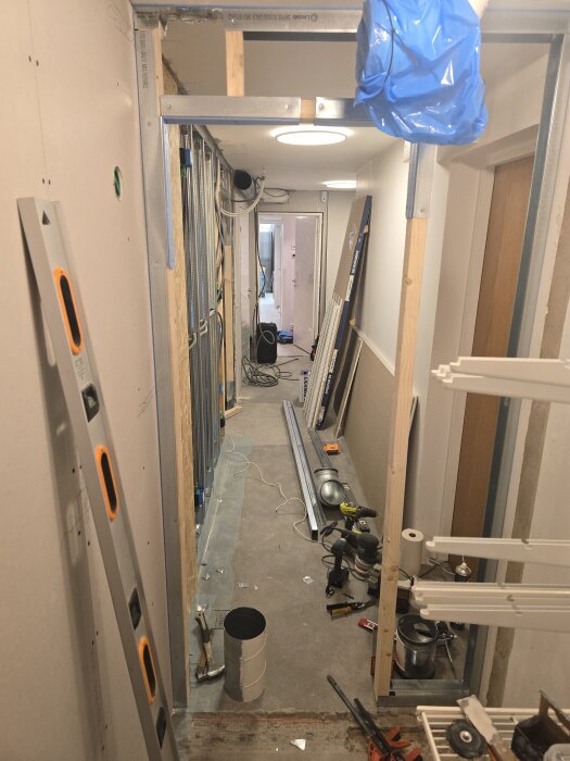 Byggarbetsplats med osb-skivor, verktyg och byggmaterial i en smal korridor under renovering av klädkammare.