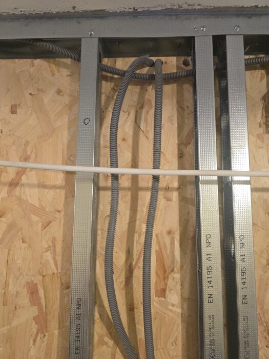 Vertikala metallreglar med dragna flexrör monterade på en OSB-vägg i ett pågående byggprojekt.