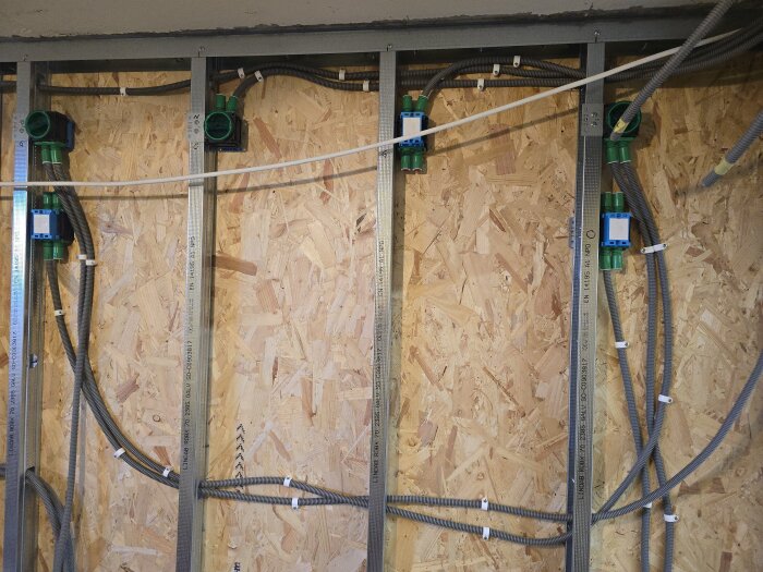 Elektriska flexrör och dosor monterade i stålskenor på en vägg av OSB-skivor under byggprojekt för klädkammare.