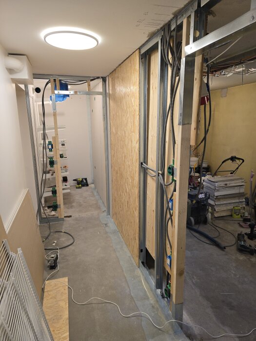 Renoveringsprojekt med stålskenor, träreglar och OSB-skivor monterade på väggar. Synliga elrör och verktyg på golvet, under installation.