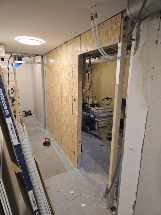 Klädkammarens väggkonstruktion med OSB-skiva, träreglar och vertikal skena, kabeldragning och utrustning på golvet.