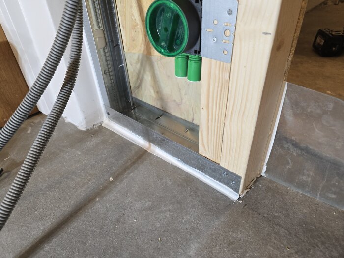 Vertikal skena och träregel vid dörröppning, flexrör och grön elinstallationsbox monterade på OSB-skiva, del av väggkonstruktion.