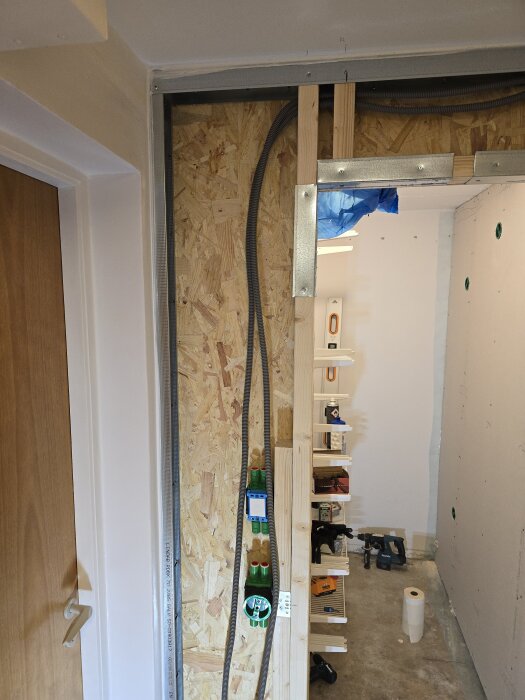 Vertikal skena i väggbygge med träregel och OSB, flexrör monterade. Verktyg och material synliga vid sidan, del av klädkammarväggens konstruktion.