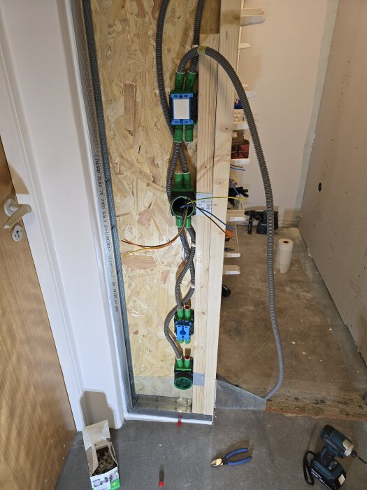 Elektrisk installation med flexrör, kabeldosor och vertikal skena inbyggd i vägg av OSB-skivor under renovering av klädkammare.