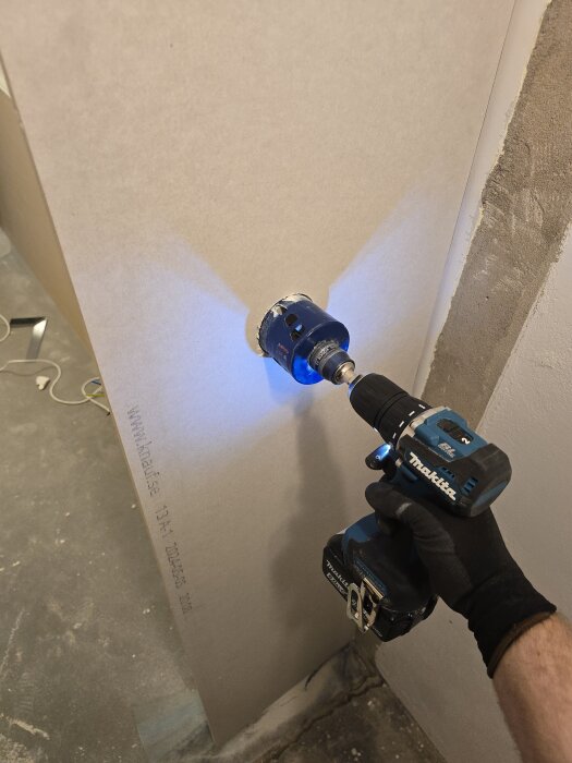 Person borrar med en hålsåg på skruvdragare i en gipsskiva, förbereder hål för eldosor i en pågående renovering.