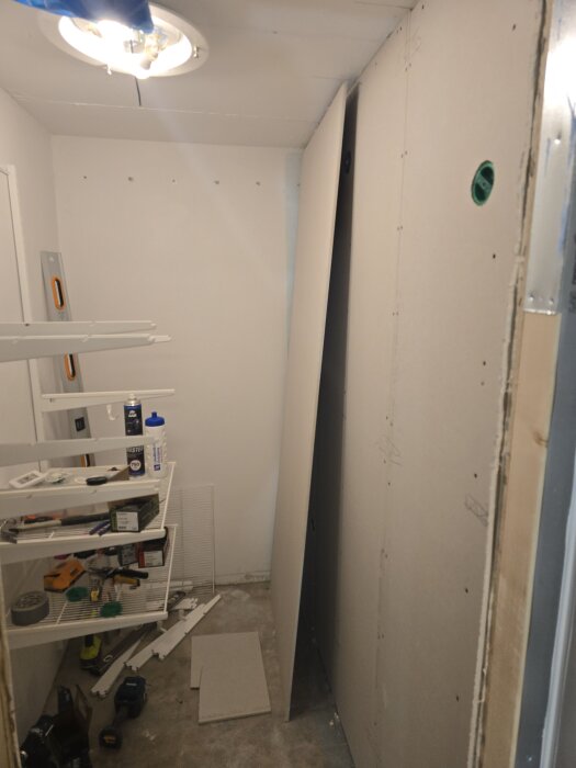 Gipsskivor monterade i liten klädkammare, omgiven av verktyg och byggmaterial på hyllor, del av renoveringsprojekt.