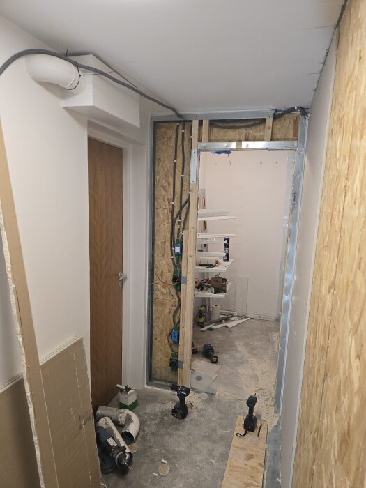 Renoveringsprojekt i korridor med synliga flexrör nära taket, hål i vägg för elinstallationer och olika byggverktyg på golvet.