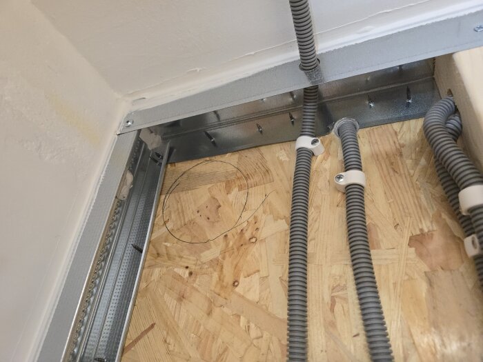 Flexrör monterade på spånskiva i byggprojekt, sedda nära ett hörn av rummet.