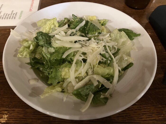Caesarsallad med romansallad och riven parmesan i en vit skål.
